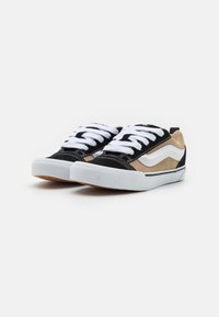 Zapatillas bajas en negro y marrón, hechas de ante y lona, con cordones blancos, rayas laterales blancas contrastantes y suela de goma.