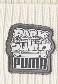 Kreem värvi kudumispea, millel on must ja hall patch, kus on kirjas "PARK SQUAD" ja "PUMA" ning kujunduselemendid rulluiskude teemal.