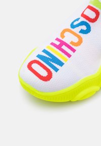 Barevné tenisky s bílým pleteným svrškem a živými nápisy v červené, růžové, modré a žluté barvě. Podešev je jasně neonově žlutá.