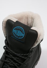Juodas odinis kulkšninis botas su švelniu, kreminės spalvos kailio pamušalu. Yra mėlyna logotipo etiketė ir juodi faktūriniai raišteliai. Nurodyta, kad yra atsparus vandeniui.