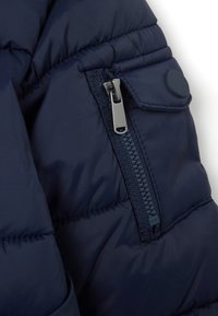 Giacca puffer blu navy in tessuto testurizzato, con zip argentata e un bottone rotondo blu navy sul colletto corto, che presenta un motivo trapuntato.