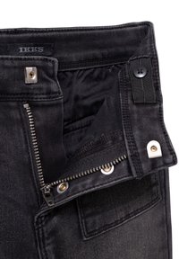 I jeans in denim neri presentano una chiusura a zip con hardware argentato, chiusura a bottone e un'etichetta all'interno della cintura. La texture è liscia e resistente.