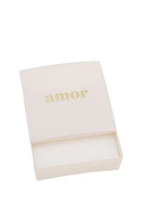 Scatola rettangolare color crema con coperchio leggermente curvo, con la parola "amor" in carattere dorato. Interno foderato con materiale morbido.