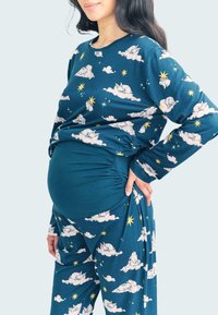 Maternity pajama set in blue with a cloud and star pattern. Long-sleeve top and loose pants, featuring stretchy ruching at the sides.