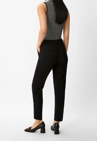 Pantalones negros de corte ajustado, con bolsillos traseros, combinados con zapatos de tacón negros. La parte superior tiene un patrón de rayas y un diseño sin mangas.