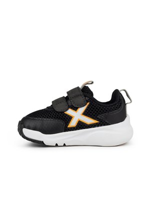 Zapatilla deportiva negra con parte superior de malla, detalles en naranja y dos correas ajustables de Velcro. Presenta una suela blanca acolchada y una puntera texturizada.
