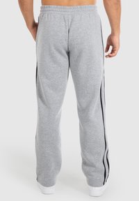 Graue Sweatpants mit einem Kordelzugbund, seitlichen Streifen und elastischen Bündchen. Der Stoff wirkt weich mit einer glatten Textur.