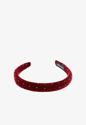 Rode fluwelen haarband met witte stippen. Gladde textuur en gebogen ontwerp. Label met de tekst "HAND MADE." Geschikt voor verschillende kapsels.