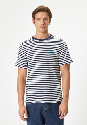 Camiseta a rayas con rayas horizontales en azul marino y blanco, cuello redondo en azul marino y gráfico azul "SEA YOU SOON" en el pecho izquierdo. Ajuste casual.