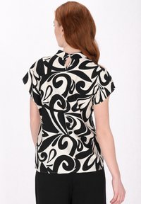 Schwarze und weiße kurzärmelige Bluse mit einem wirbelnden Blumenmuster, einem Schlüsselöffnungsdetail am Rücken und leichtem Stoff.