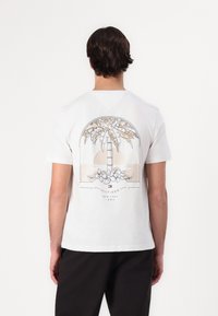 Biela bavlnená tričko s grafikou palmy a kvetinovými akcentmi a textom "HILFIGER NEW YORK 1985" v jemnej farebnej palete.