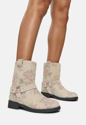 Botas de tobillo de tela texturizada con estampado floral beige, suela plana negra y correas decorativas con herrajes plateados.