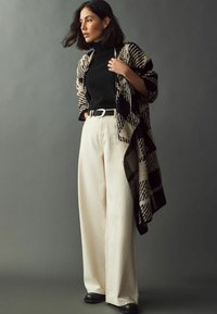Uldblandede sjaler med sort og beige ternet mønster, sort turtleneck, cremefarvede vide bukser og sorte lædersko.