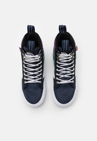 Höga sneakers med en marinblå syntetisk ovandel och gröna samt lila detaljer, vita snören och en vit gummisula.