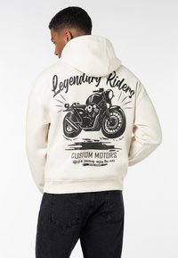 Hooded sweatshirt in cream with a black motorcycle graphic and text on the back. Features ribbed cuffs and hem, soft fabric texture.