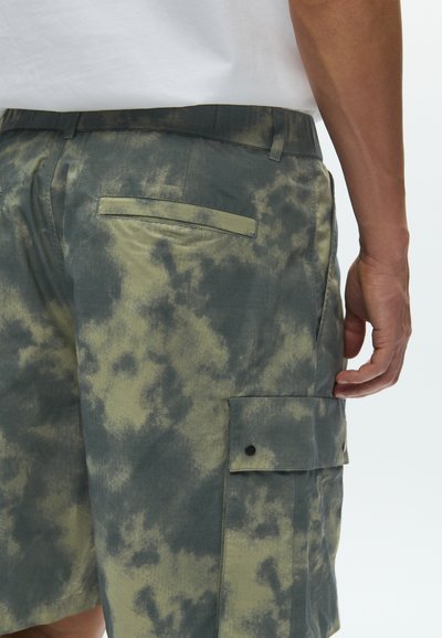 Βερμούδα cargo με καμουφλάζ, που συνδυάζει σκούρο πράσινο και ελιάς, με πλαϊνή τσέπη και πίσω τσέπη με φάσα. Υλικό από βαμβάκι-ελαστάνη.