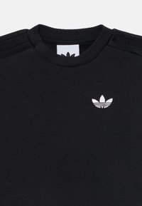 Sweatshirt noir avec col côtelé, arborant un logo trefoil blanc brodé. Trois bandes noires sur les épaules. Matière en coton douce.