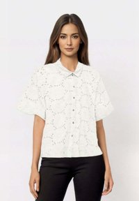 White short-sleeve shirt with a button-down collar, featuring embroidered eyelet patterns. Paired with black pants, medium texture.