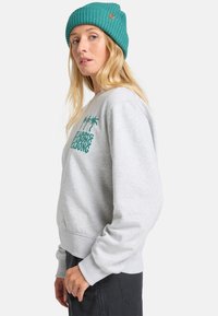 Grijze sweatshirt met geribde manchetten en zoom, met groene grafische tekst en palmbomen. Draagt een teal gebreide beanie.