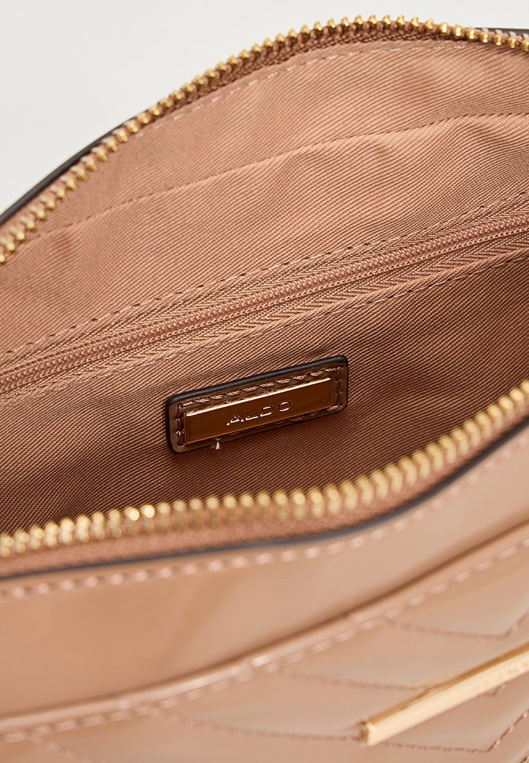 Intérieur d'un sac à main beige matelassé avec doublure en tissu, fermeture éclair dorée et petite étiquette en cuir embossée du nom de la marque "ALDO."