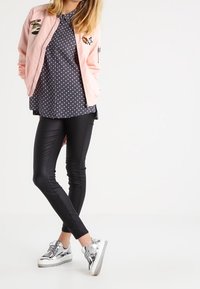 Różowa kurtka bomberka z naszywkami, niebieski top w groszki, czarne legginsy i srebrne trampki, prezentujące casualową, warstwową stylizację.