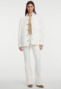 Witte denim overhemd met drukknoopsluiting, gecombineerd met een beige tanktop en witte flared pants. Opmerkelijke details zijn een borstzak en een gladde textuur.