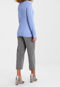 Lichtblauwe kabelgebreide trui met geribbelde zoom, gecombineerd met grijze, getextureerde cropped broek en zilveren schoenen met hoge, blokhakken.