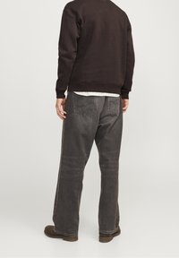 Jeans de pierna ancha gris oscuro con un corte relajado, que presentan bolsillos traseros y una textura ligeramente descolorida, combinados con un sudadera marrón.