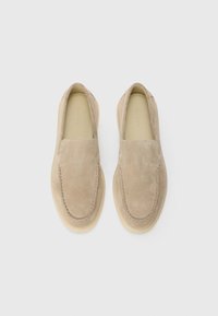 Ein Paar beige Wildleder Slipper mit leichten Gummisohlen, von oben betrachtet vor einem schlichten weißen Hintergrund.