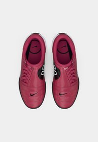 Sarkanas ādas sporta apavus ar melniem elementiem, kurus raksturo teksturēta virsma, apaļa purngala forma un auklu aizdare. Sānā redzams Nike logo.