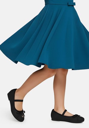 Czarne baletki z paskami, okrągłymi noskami i małą kokardką z przodu, zestawione z turkusową rozkloszowaną sukienką.