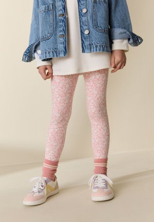 Kind draagt roze en witte bloemenlegging, roze sokken, pastelgekleurde sneakers, wit lang shirt en blauwe spijkerjas met opgerolde mouwen.