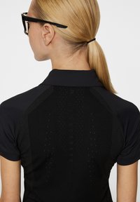 Czarna koszulka polo sportowa o dopasowanym kroju. Zawiera teksturowane panele i subtelne logo z tyłu. Krótkie rękawy, nowoczesny kołnierz.