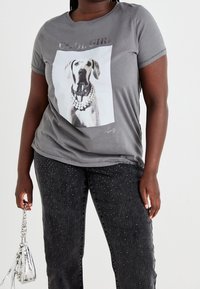 Harmaa t-paita, jossa on koira-aiheinen grafiikka ja "Cool Girl" -teksti, lyhyet hihat ja rento leikkaus. Yhdistetty mustiin farkkuihin, joissa on kimaltavia yksityiskohtia.