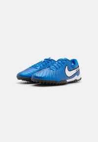 Blue synthetic soccer shoes with textured surface, black rubber outsole, and white Nike swoosh on the side. Lace-up design for secure fit.