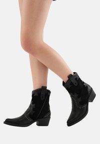 Botines negros de tobillo con una combinaci�ón de cuero y ante, que presentan cortes decorativos, tachuelas metálicas, un zipper lateral y un tacón bajo.