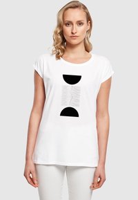 Hvid bomulds t-shirt med opsmøgte ærmer, der har et sort grafisk design bestående af halvcirkler og bølgede linjer trykt på forsiden.