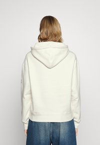Sweat à capuche blanc à coupe décontractée, avec une poche kangourou et des poignets côtelés. Matière douce avec un design minimaliste.