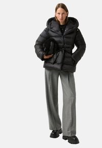Black puffer jacket with a hood and belt detail, paired with gray wide-leg trousers and black platform shoes. Holding a black faux fur bag.
