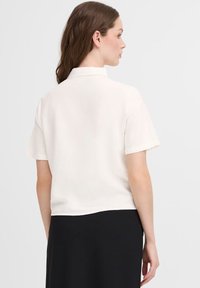 Blusa bianca a maniche corte con collo e vestibilità rilassata, realizzata in tessuto leggero, caratterizzata da una consistenza liscia e da un design cropped.