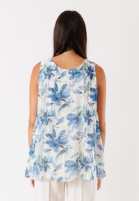 Top senza maniche realizzato in tessuto leggero, con un motivo floreale blu su uno sfondo bianco, con scollatura rotonda e vestibilità morbida.