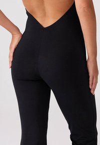 Czarny dopasowany body z głębokim dekoltem z tyłu, wykonane z elastycznej tkaniny. Gładka struktura bez widocznych wzorów czy detali sprzętowych.