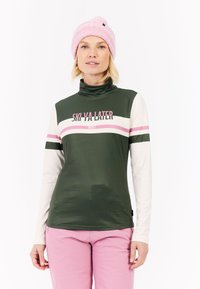 Zeleni dugi rukav s ružičastim i bijelim prugama, visokim ovratnikom i tekstom "SKI YA LATER". Upareno s ružičastim hlačama i svijetlo ružičastom beanie kapom.