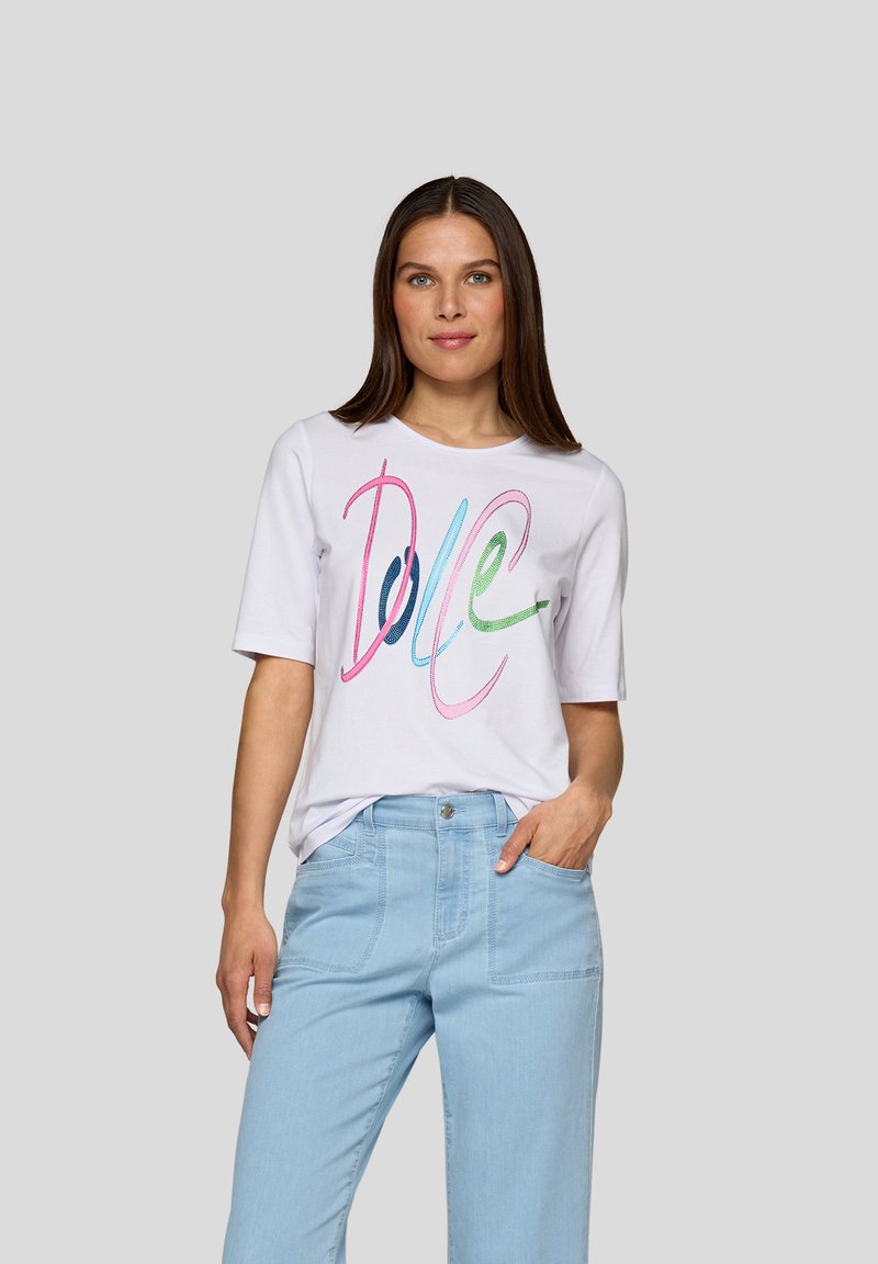 White cotton t-shirt with short sleeves featuring colorful embroidered text "DOLCE" in pink, green, and blue. Paired with light blue trousers.