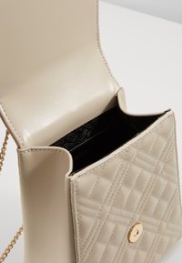 Borsa a tracolla in pelle trapuntata beige con dettagli in oro, dotata di una catena come manico e una pattina aperta che rivela un rivestimento interno nero.