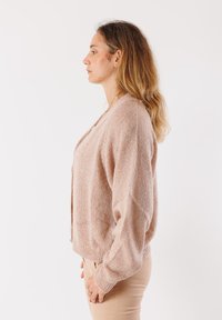 Cardigan rosa chiaro realizzato in filato testurizzato, con una vestibilità morbida, maniche lunghe e scollo a V. Leggera lucentezza su tutta la stoffa.
