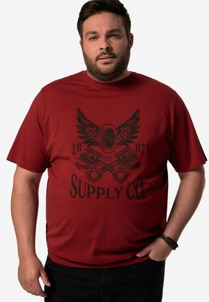 Červené bavlněné tričko s černým grafickým designem, který zobrazuje křídla, písty a text "Supply Co." Volný střih s krátkými rukávy.