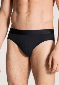 Schwarze Baumwollunterhose mit glatter Textur, elastischem Bund mit "CALIDA"-Logo und klassischem Schnitt. Die Vorderseite hat ein konturiertes Täschchen-Design.
