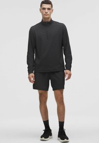 Juodas sportinis kostiumas, susidedantis iš ilgomis rankovėmis marškinėlių su ketvirtiniu užtrauktuku ir atitinkančių šortų, turinčių tekstūruotą medžiagą ir priglundantį dizainą.