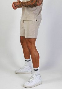 Beige bomull t-shirt och shorts med sidofickor, parat med vita högskurna sneakers och svarta randiga knästrumpor.